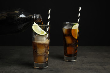 Pouring refreshing soda drink into glass on grey table against black background