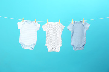 Colorful baby onesies hanging on clothes line against blue background. Laundry day