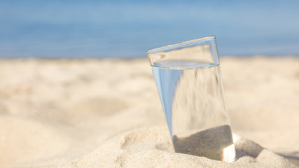 Sandy beach with glass of refreshing drink on hot summer day, space for text