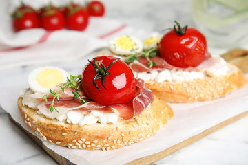 Cutting board of delicious bruschettas with prosciutto on white marble table