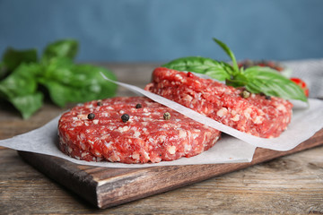 Raw meat cutlets for burger on wooden table against blue background, closeup