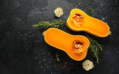 Fresh Butternut squash with rosemary, garlic, chilli flake and salt on black rustic background