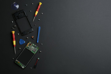 Disassembled mobile phone and repair tools on black background, flat lay. Space for text