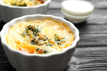 Tasty broccoli casserole in ramekin on black wooden table, closeup