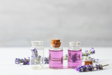 Bottles with essential oil and lavender flowers on white wooden table