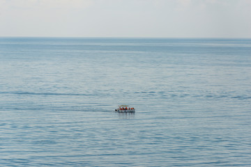 Aerial view on a white floating boat with people in it in the blue black sea