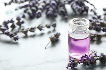Bottle of natural essential oil and lavender flowers on light background