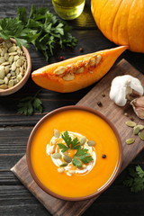 Delicious pumpkin soup in bowl on wooden table, flat lay