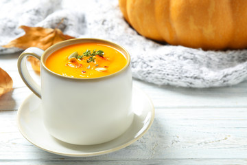 Delicious pumpkin soup in cup on white wooden table