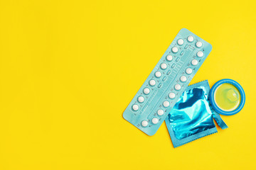 Condoms and birth control pills on yellow background, flat lay with space for text. Safe sex concept