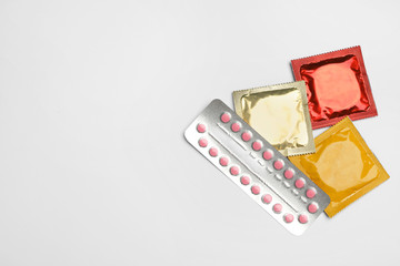 Condoms and birth control pills on light grey background, flat lay with space for text. Safe sex...