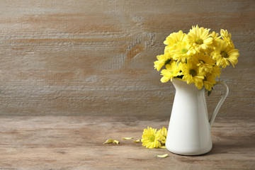 Jug with beautiful chamomile flowers on wooden table. Space for text