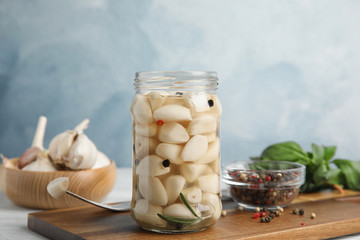 Composition with jar of pickled garlic on white table against blue background