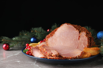 Plate with Christmas ham on grey table against black background