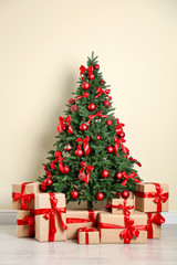 Fototapeta na wymiar Decorated Christmas tree and gift boxes near beige wall