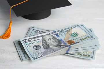 Dollar banknotes and student graduation hat on white wooden background. Tuition fees concept