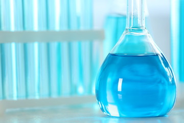 Volumetric flask with light blue liquid on table, closeup. Space for text