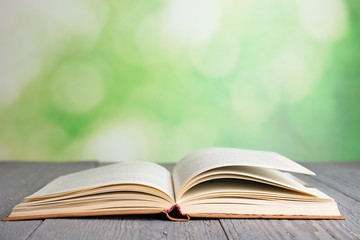 Open book on grey wooden table against blurred green background. Space for text