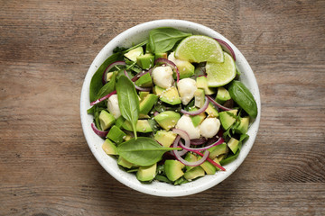 Delicious avocado salad with mozzarella on wooden table, top view