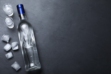 Bottle of vodka, ice cubes and shot glasses on black table, flat lay. Space for text