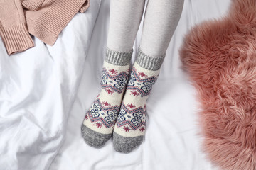 Woman wearing knitted socks on white fabric, top view. Warm clothes
