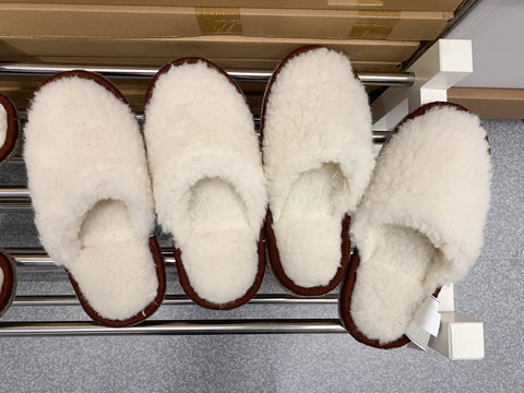 Two Pairs Of Cozy Fuzzy White Home Slippers On A Metal Shelf