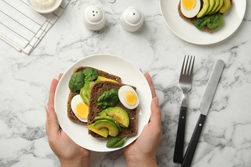 Woman with tasty avocado toasts at white marble table, top view