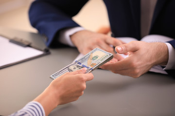 Young woman giving dollar bills to businessman in office, closeup