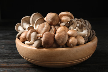 Different fresh wild mushrooms in bowl on wooden table