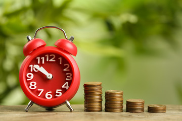 Red alarm clock and stacked coins on wooden table against blurred background. Money savings