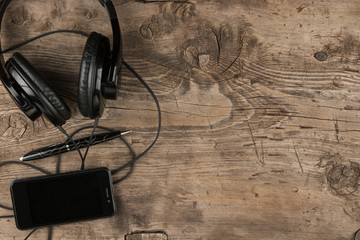 Phone, pen and headphones lying on a wooden background. With space for your text.