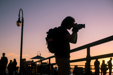 A young male photographer photographs the sunset from the Santa Monica Pier.