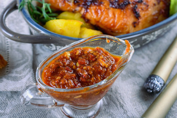 Delicious tomato pesto in a glass gravy boat next to a hot lunch dish, close up