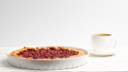 Homemade galette with red raspberries and black currants and cup of coffee on white wooden table. Front view. Copyspace.