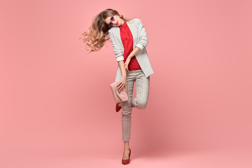 Fashion. Beautiful woman in autumn jacket, trendy hairstyle, make up dance. Adorable well dressed blonde girl on pink. Gorgeous fashionable lady in red, hairstyle, makeup. Creative beauty shot