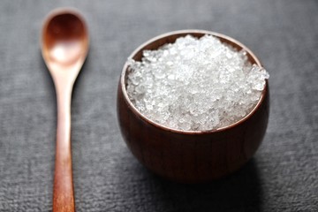 dead sea salt in bamboo bowl with wooden spoon on dark gray background closeup