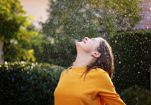 Happy cheerful teenage girl enjoying rain and sun putting her face under water drops smiling happily. True happiness. Summer lifestyle.