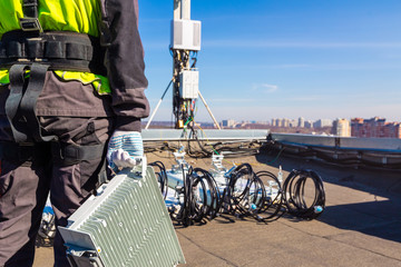 Professional industrial climber in uniform with telecomunication equipment in his hand and antennas...
