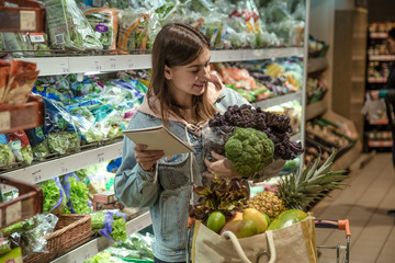 A young woman with a notebook buys groceries in the supermarket.