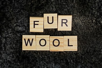 the word from wooden letters lies on a black gray fur of woolen clothes