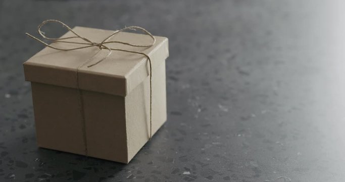 Slow motion man hand bring brown paper gift box on terrazzo countertop