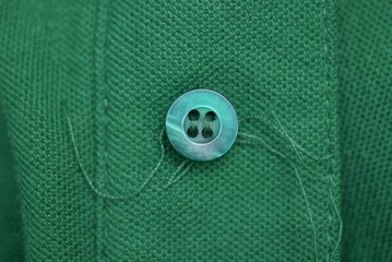 one plastic button with threads on a green cloth