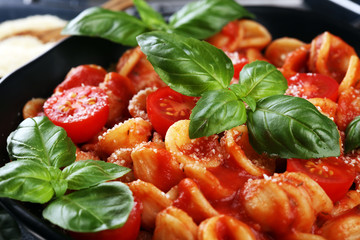 Pasta orecchiette. Plate of delicious orecchiette with tomato sauce garnished with parmesan cheese and basil on rustic background