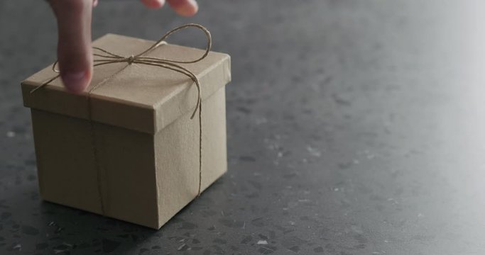 Slow motion man hand bring brown paper gift box on terrazzo countertop