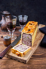Traditional French Pate en croute with goose meat and liver as closeup with red wine on a wooden board