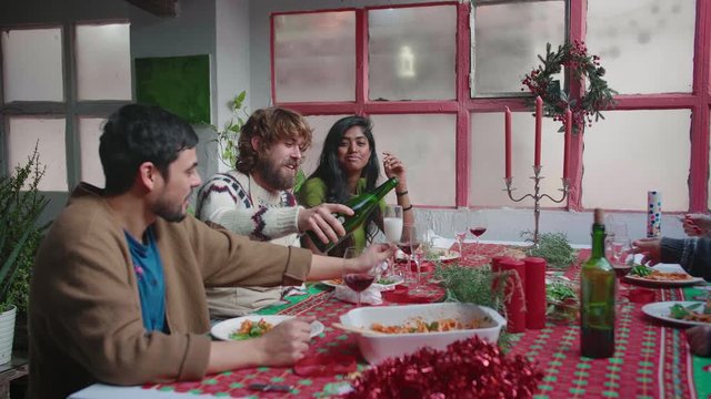 Party Celebration Together Gathered at Table happy yong joyful friends are laugthing and smiling serving champain or drinks to glasses Eating, Drinking, Joking and Having Fun togeter at christmas or