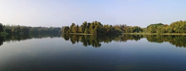 Fototapeta premium Reflection of trees in the lake during fall season - panormic view