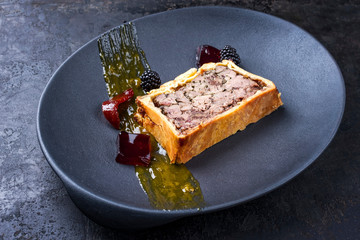 French pate en croute with goose liver, fruit relish and jelly as closeup on a modern design cast...