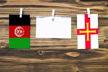 Hanging flags of Afghanistan and Guernsey attached to rope with clothes pins with copy space on...