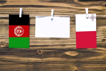 Hanging flags of Afghanistan and Malta attached to rope with clothes pins with copy space on white...